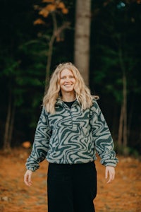 a woman in a gray zebra print sweatshirt standing in the woods